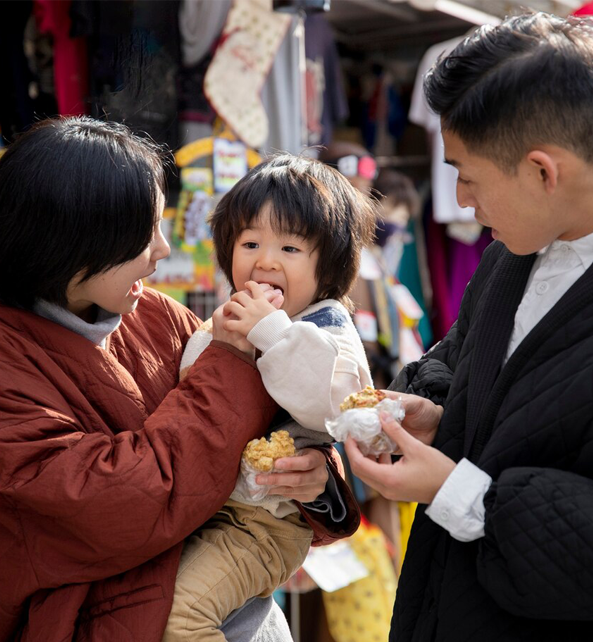 A mother feeding her kid while carrying her and a father holding a food.