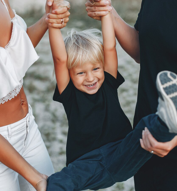 A child having a good time while he was swinging in his arms by his parents.